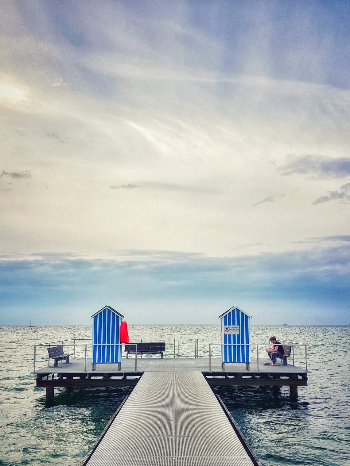 Blick auf das Meer mit Badestelle und einem Mann auf der Bank sitzend