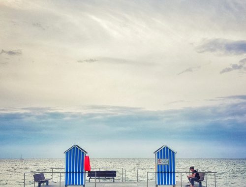 Blick auf das Meer mit Badestelle und einem Mann auf der Bank sitzend